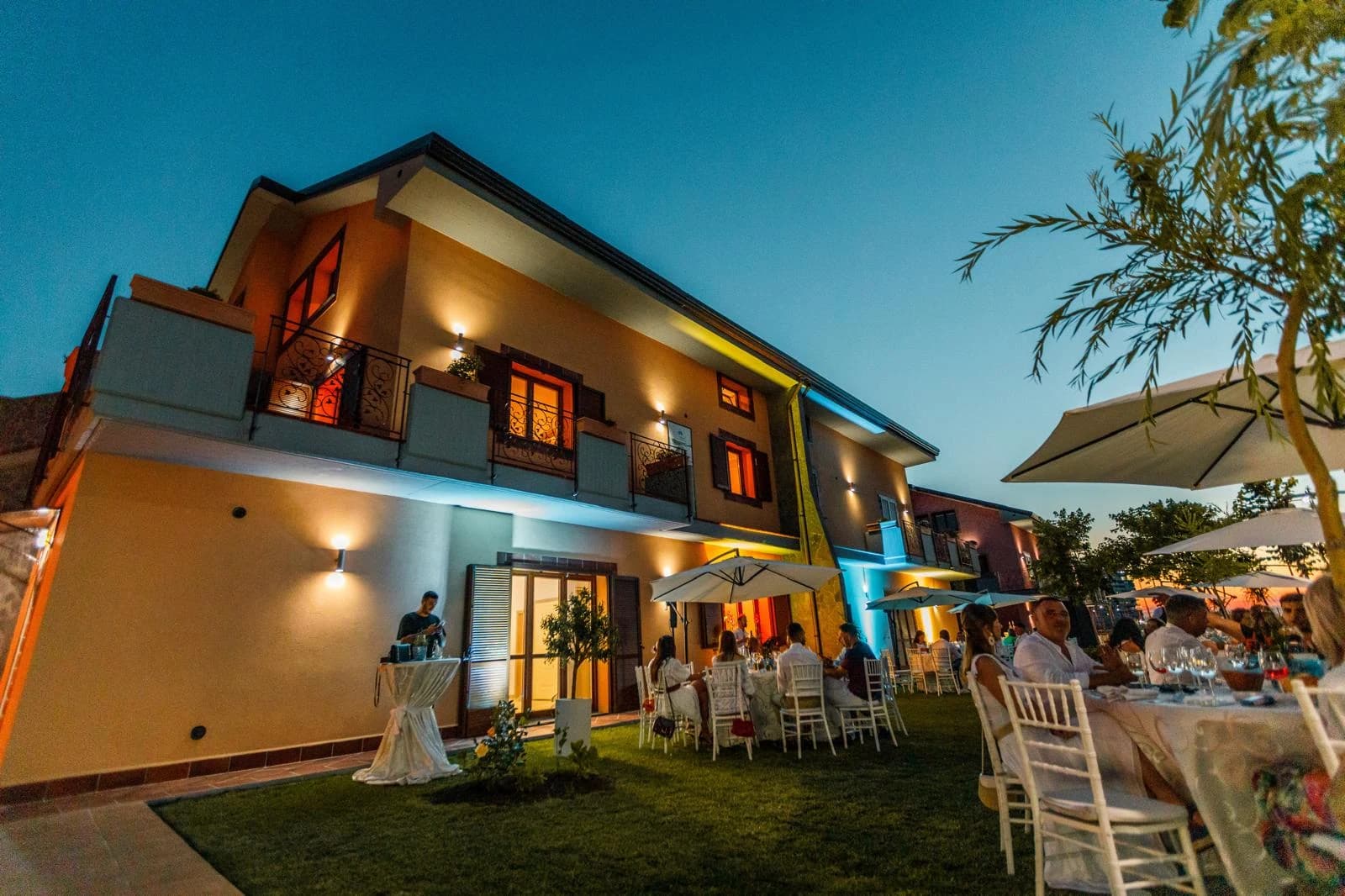 Fațada Vilei D'Oro la lăsarea serii, cu invitați la mese în grădină